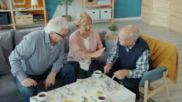 Old men and woman playing lotto doing high-five showing thumbs-up in house - Video, Çekim