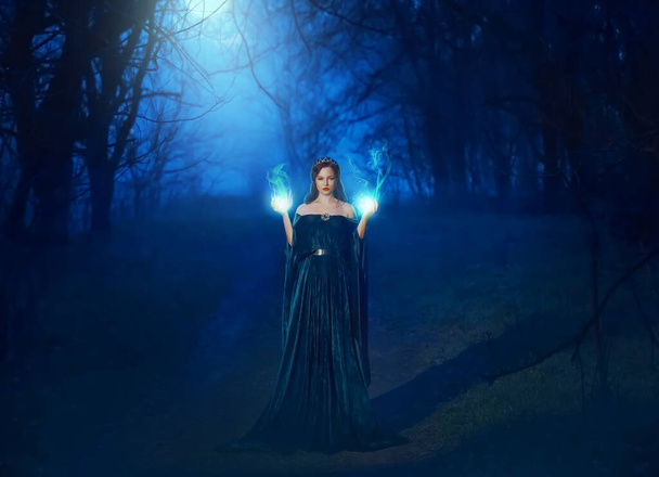Mystic beauty woman evil witch in dark night fog forest blue moon light. Hands burning magic spell fire. Vampire queen demon power face. Vintage medieval dress cape. Scary Lady Halloween style clothes - Photo, image