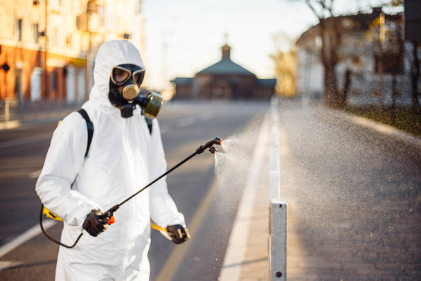 Disinfection team worker is cleaning pavement fence with a sterilizing water spraying it over the coronavirus infected surface. Covid-19 protective equipment and actions to stop spread of the disease - Photo, Image