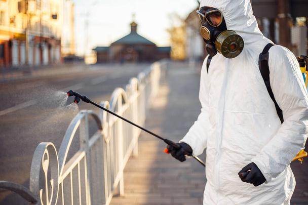 Disinfection team worker is cleaning pavement fence with a sterilizing water spraying it over the coronavirus infected surface. Covid-19 protective equipment and actions to stop spread of the disease - Photo, Image