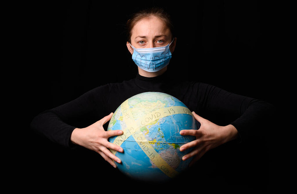 Woman hands holding the Earh globe in the hands. Woman in the doctor breath medicine mask. Coronavirus protection for people all continents and the world. Isolated on a black background. Concept stop covid-19. - Фото, зображення