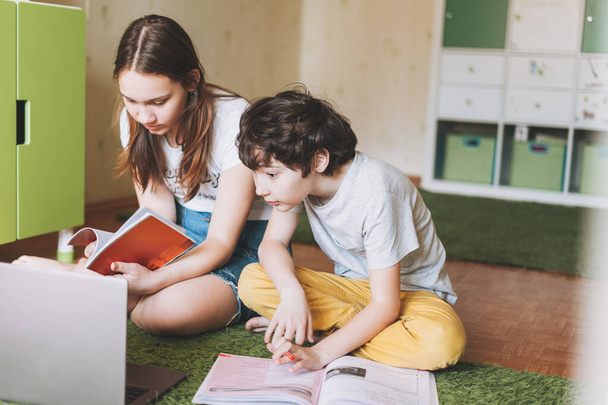 Siblings brother sister attractive girl teenager and tween boy do homework learn foreign language writing in pupil book with opened laptop at the room home dictance education. - Photo, Image