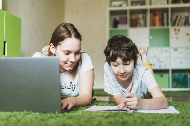 Siblings brother sister attractive girl teenager and tween boy do homework learn foreign language writing in pupil book with opened laptop at room home dictance education. - Photo, Image