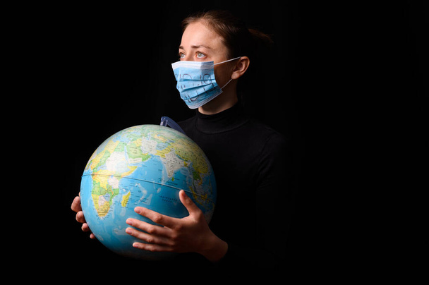 Woman hands holding the Earh globe in the hands. Woman in the doctor breath medicine mask. Coronavirus protection for people all continents and the world. Isolated on a black background. Concept stop covid-19. - Foto, immagini