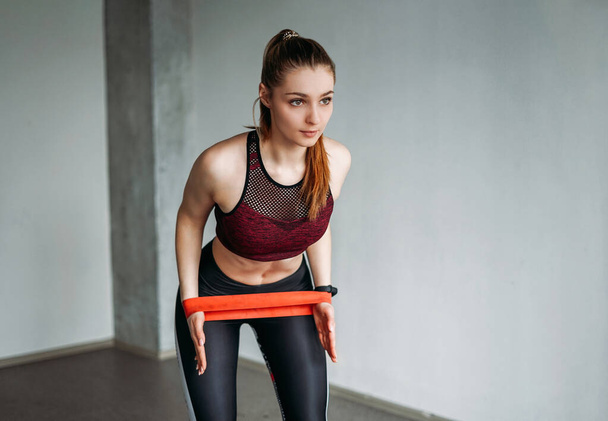 Atraktivní fit mladá žena sportovní oblečení fitness dívka dělá strečink s elastickou kapelou na podkroví studio cvičení třídy - Fotografie, Obrázek