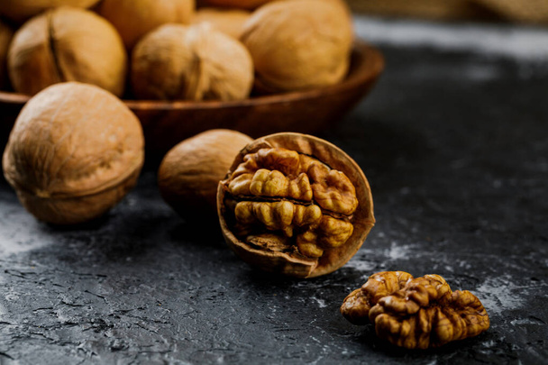 peeled walnut and plate with some raw walnuts on dark table. - Photo, Image