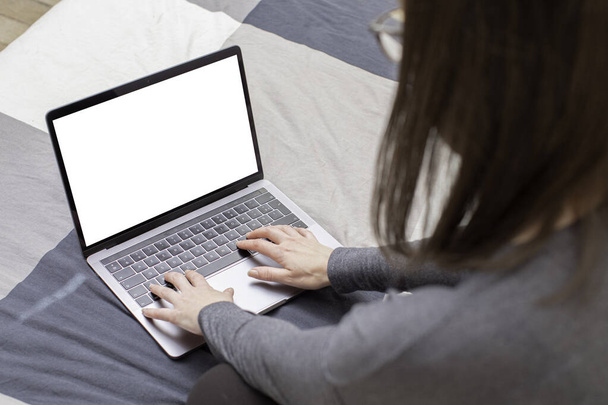 Young woman surfing on her metallic gray laptop and looking for informations on the internet. She has long brown hair, glasses and a gray sweater, and she sits on a plaid patterned sheet - Photo, Image