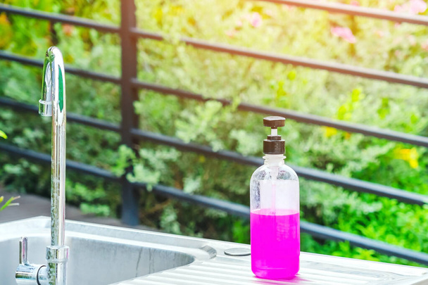 Butelka z różowym żelem nasączonym alkoholem lub antybakteryjny dezynfektor mydła na zlewozmywakach aluminiowych w ogrodzie, żel nasączony alkoholem do czyszczenia dłoni w celu zapobiegania rozprzestrzenianiu się zarazków i bakterii oraz zapobiegania zakażeniom wirusem korony (covid-19) - Zdjęcie, obraz