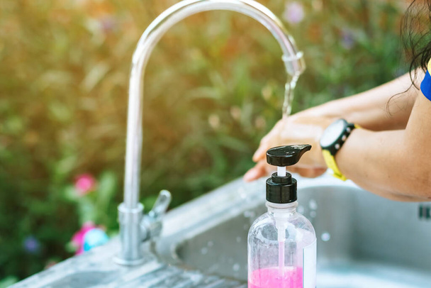 アルミ製の浴槽にピンクの石鹸でタップから手を洗う女性。インフルエンザウイルスの概念, Covid-19 (コロナウイルス病).石鹸ボトルの選択的焦点. - 写真・画像
