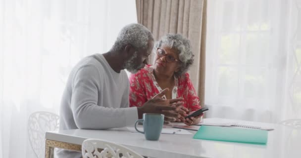 A senior African American couple spending time at home together, social distancing and self isolation in quarantine lockdown during coronavirus covid 19 epidemic, sitting at a table, using a calculator and talking in slow motion - Video, Çekim