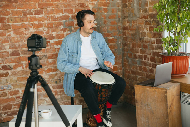 Caucasian musician playing hand drum during online concert at home isolated and quarantined, inspired improvising - Photo, image