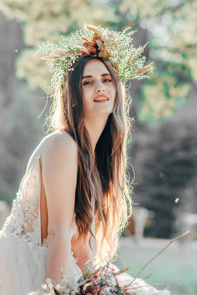 portrét krásné nádherné šťastné brunetky nevěsty se stylovou kyticí a věnečkem. Přírodní make-up, účes, věnec. nevěsta v lese s kyticí sušených květin. umělecká fotografie - Fotografie, Obrázek