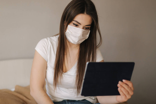 Young woman in mask use tablet on the bed. Female watch online video during quarantine. Student Study at home - Foto, afbeelding
