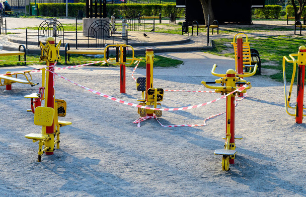 An empty sport playground, whose exercisers wrapped with a warning red and white tape. Forbidden to visit during the quarantine period of the pandemic of COVID-19 disease caused by coronavirus - Photo, Image