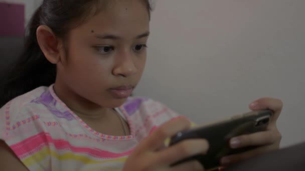 Rozkošná dívka hraje hry na mobilním smartphonu a sedí na pohovce během karantény doma. Asijské dospívající teenager textování na sociální on-line komunikaci s mobilním telefonem v obývacím pokoji. - Záběry, video