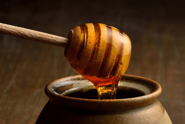 Miele versando da tuffatore miele di legno in tazza di ceramica. Vasetto di terracotta per miele su tavola di legno. - Foto, immagini