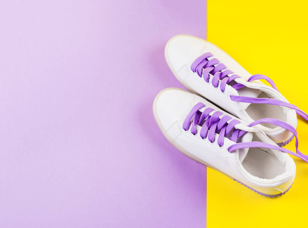 Witte sneakers met paarse veters op gele achtergrond - Foto, afbeelding