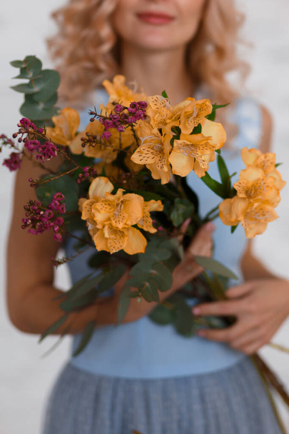 A beautiful floral bouquet is held by a young girl who is blurred. She is wearing a blue dress.Selective focus. Medium sharp  - Zdjęcie, obraz