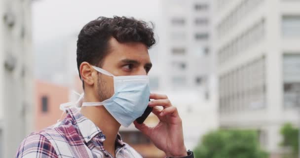 Portrait d'un homme caucasien portant un masque facial contre le coronavirus, 19 ans dans les rues de la ville pendant la journée, parlant sur son smartphone
. - Séquence, vidéo