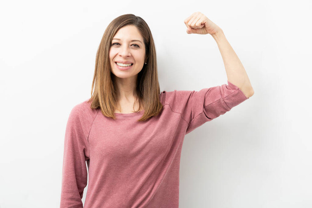 Happy Caucasian woman dressed casual and flexing her arm showing her strength and smiling - Photo, Image
