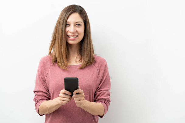 Portret ładnej brunetki trzymającej smartfona i nawiązującej kontakt wzrokowy w studiu - Zdjęcie, obraz