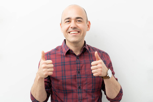 Blanke man geeft duimen op als teken van sympathie en goedkeuring met een glimlach in een studio - Foto, afbeelding