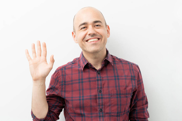 Amistoso hombre caucásico saludando y saludando con su mano y sonriendo en un estudio
 - Foto, imagen