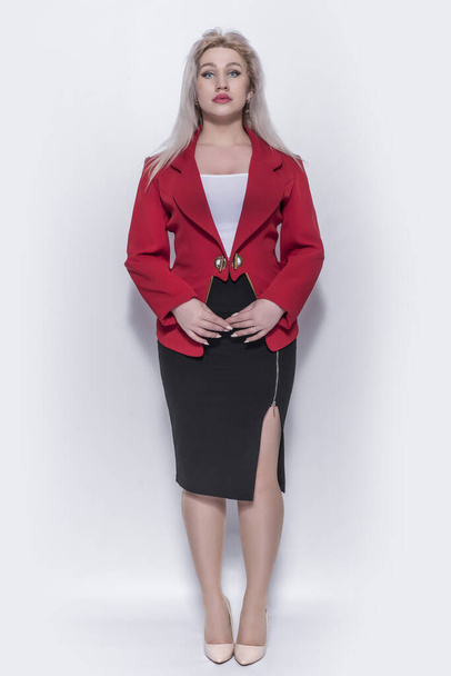 Beautiful young girl, blonde, business woman in a red jacket and suit on a gray background. - Valokuva, kuva