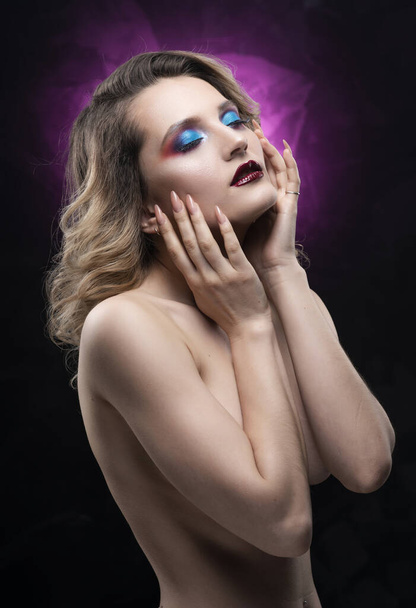Beautiful topless busty girl with blue makeup poses on black and pink background, covering her breast with her hands. Fashionable, advertising and commercial portrait design - Foto, Bild