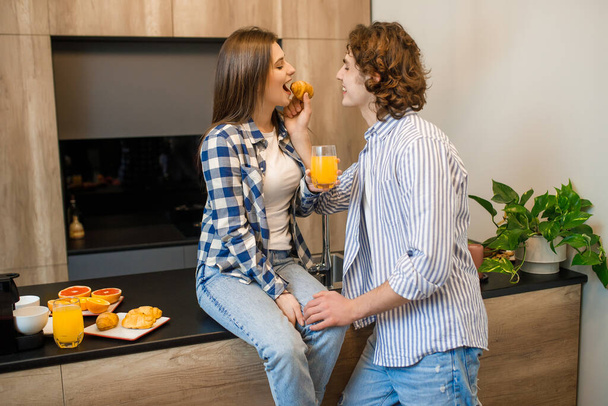 Young cheerful couple having fun , feeding each other during breakfast time in the kitchen. - Foto, imagen