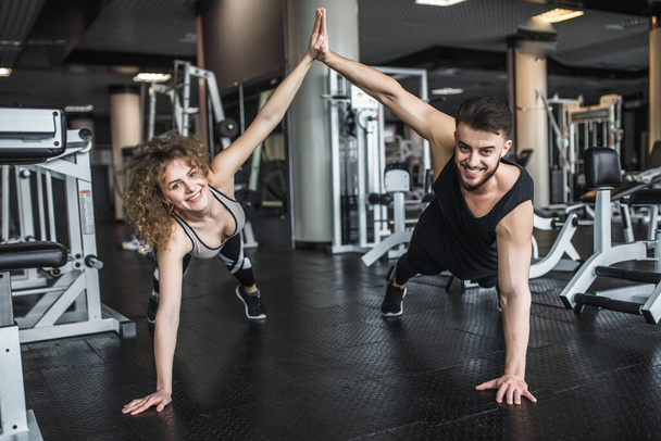 Motivated young blond woman and man trainer in middle of workout, standing in plank with give five hands. - Foto, imagen
