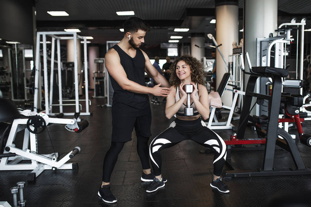 Belle jeune entraîneuse sportive et femme avec haltère dans la salle de gym pendant l'entraînement
. - Photo, image
