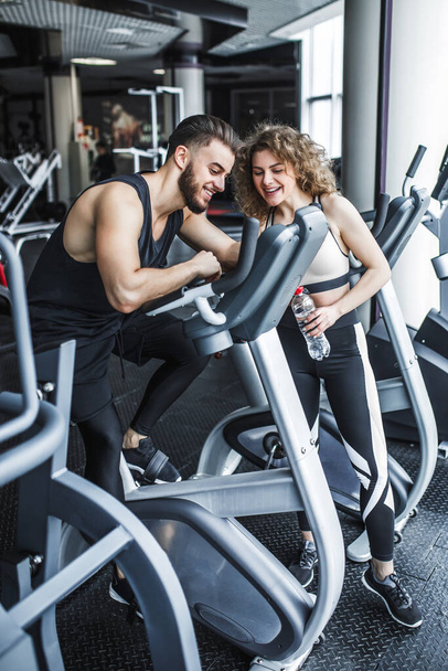 A man and a woman are watching a training video. A group of two young people watching a video about exercise on a tablet. Man resting after workout sitting on the sports equipment in the gym. - Foto, afbeelding