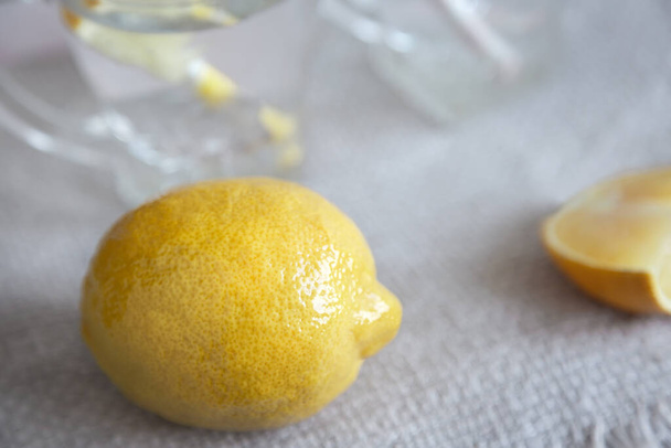 Lemon a kousek citronu na stole na ubrousku. V brýlích na pozadí pro výrobu citrónového nápoje. Prezentováno na světlém pozadí. Mezera pro kopírování. - Fotografie, Obrázek