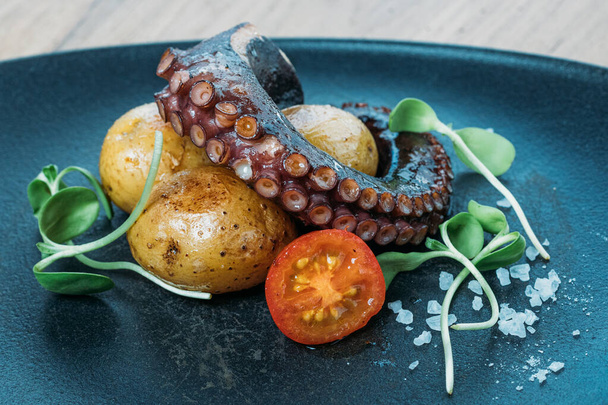 tentacules de poulpe grillé, servi avec des pommes de terre et des tomates légumes sur une assiette bleue dans un restaurant
 - Photo, image