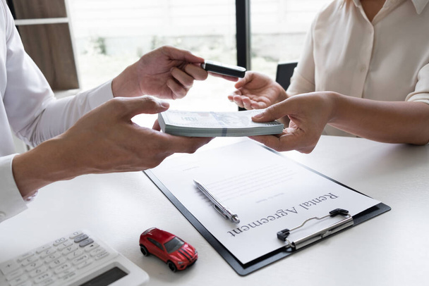 Klant betaalt de huurprijs aan een autoverhuurbedrijf na ondertekening van een autohuurovereenkomst in het kantoor, Autoverhuur concept. - Foto, afbeelding