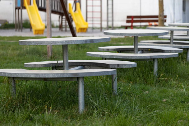 Fila de mesas vacías al aire libre y bancos rodeados de césped cubierto en un parque urbano debido al cierre del coronavirus o pandemia de Covid-19
 - Foto, imagen