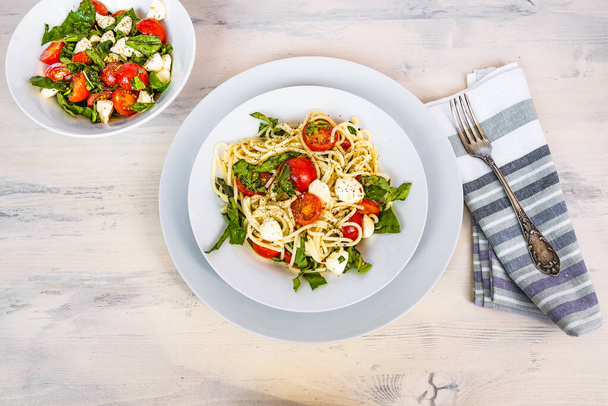 Italiaans eten - Spaghetti caprese in een bord op een lichte rustieke achtergrond, bovenaanzicht. Pasta met mozzarella, kerstomaten en basilicum - Foto, afbeelding