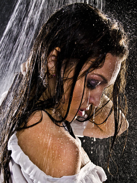 Conceptual view and scene of a young, sensual, beautiful girl, a woman who washes in the shower under a powerful jet of water in the backlight in an aqua studio on a dark background. - 写真・画像