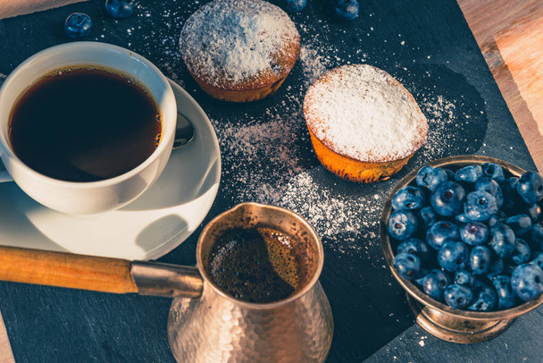 Delicioso desayuno - una taza de café y magdalenas con arándanos en bandeja de pizarra
 - Foto, imagen