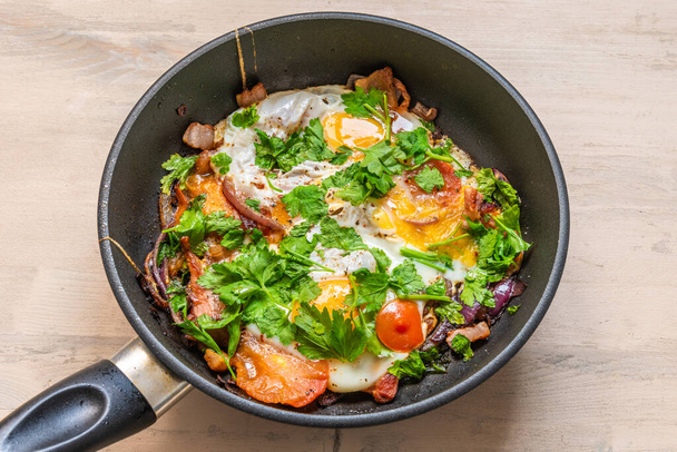 Świeże rustykalne śniadanie - smażone jajko z bekonem, cebulą i pomidorami wiśniowymi na patelni - Zdjęcie, obraz