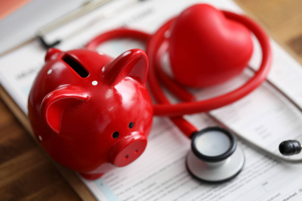 Red piggy bank stethoscope and toy heart lying at health insurance claim form - Foto, Imagem