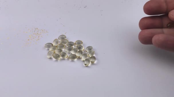 Ein Mann wirft eine Handvoll Vitamin-D3-Gelatine-Tabletten auf den Tisch. Kapseln isoliert auf weißem Hintergrund - Filmmaterial, Video