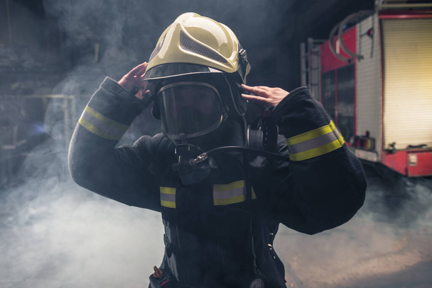 Ritratto di un pompiere che indossa affluenze da pompiere e casco. Sfondo scuro con fumo e luce blu. - Foto, immagini