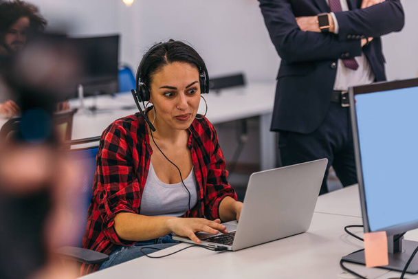 Πορτρέτο μιας όμορφης νεαρής γυναίκας που φοράει ακουστικά και χαμογελά ενώ εργάζεται στο laptop - Φωτογραφία, εικόνα
