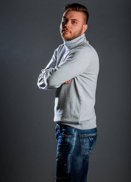 Attractive young stylish man posing in knitted polo neck jumper and denim pants - Foto, afbeelding