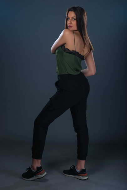 Portrait d'une jeune femme sexy debout dans un studio et portant un haut vert foncé et un pantalon noir - Photo, image