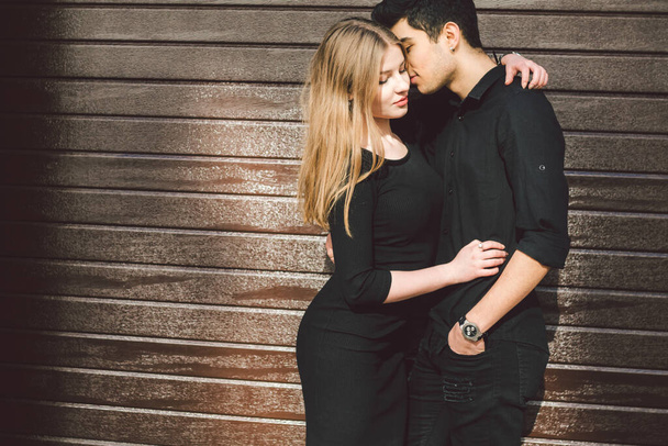Stilvolles Paar in schwarzer Kleidung posiert auf einem Hintergrund einer Holzwand. Türkischer Typ und kaukasische Frau Date und Liebe. Lifestyle Stilvolles Liebespaar. Jung und frei. - Foto, Bild