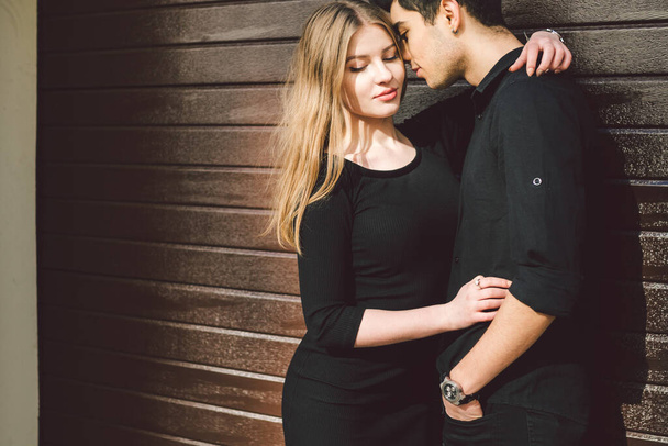 Stilvolles Paar in schwarzer Kleidung posiert auf einem Hintergrund einer Holzwand. Türkischer Typ und kaukasisches Mädchen Date und Liebe. Muslimischer Mann und Frau zusammen. - Foto, Bild