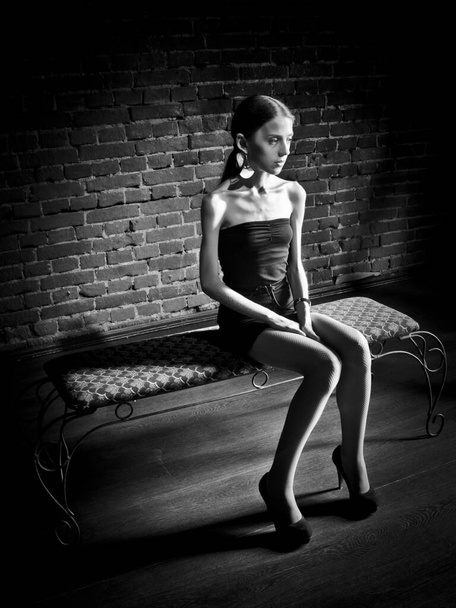 Conceptual portrait of a young, seductive, emotional, thin and beautiful girl, a woman in a dark dress and a dark studio, in the interior. - Photo, image
